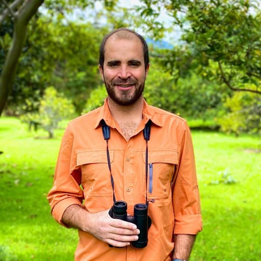 A man wearing an orange birding shirt and pair of binoculars